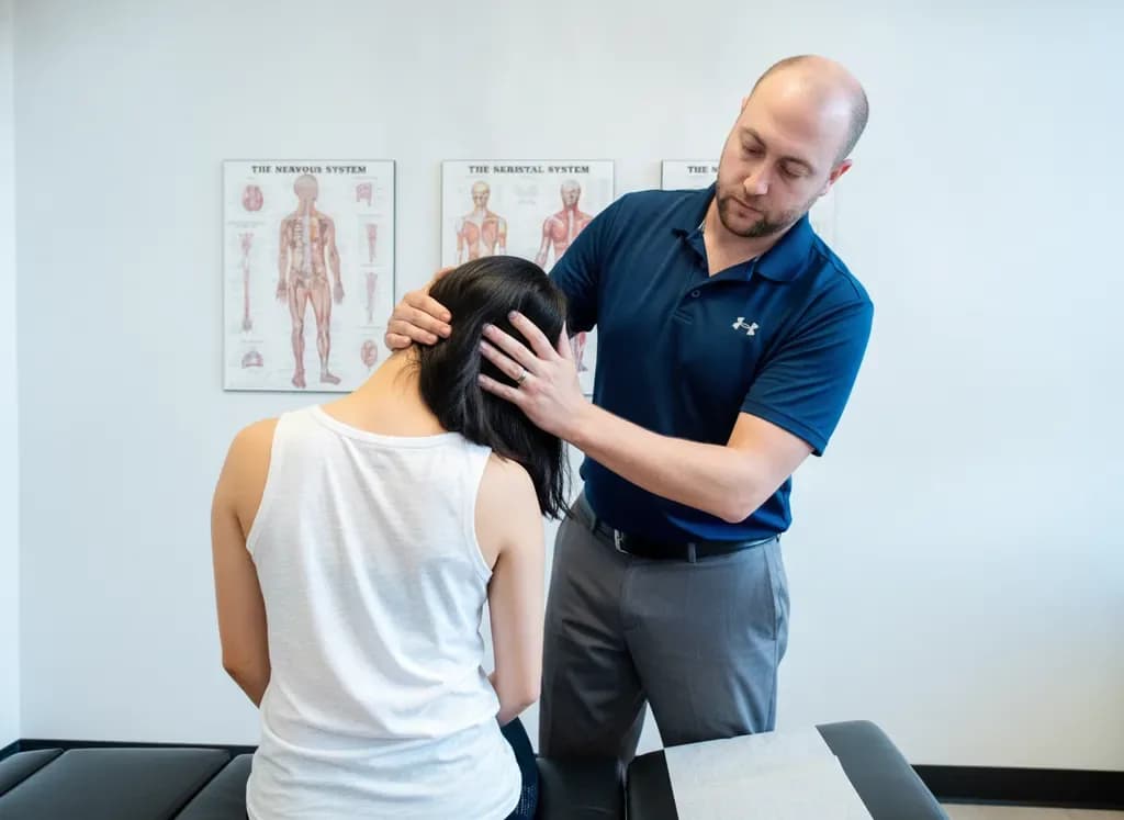 Chiropractor guiding a patient's lateral neck flexion from behind during a neck pain assessment at Back In Balance Clinic, downtown Toronto